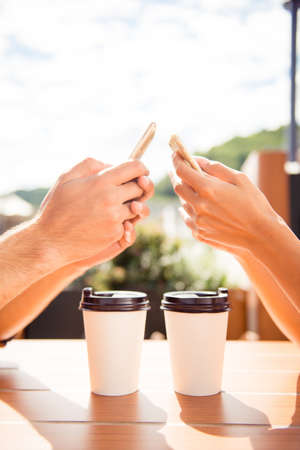 Close up of man and woman chatting in cafe with cups of coffee at sunny summer morning