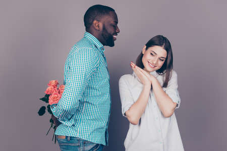 Handsome afro american guy hide flowers from beautiful caucasian girl