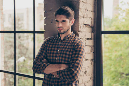 Minded bearded young confident man with crossed hands near windowの写真素材