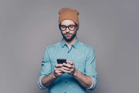 Handsome young man in yellow hat and glasses typing smsの写真素材