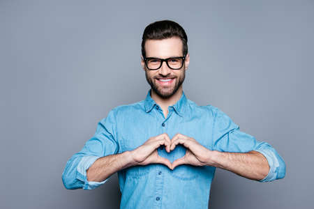 Portrait of happy handsome man in glasses making heart with fingersの写真素材