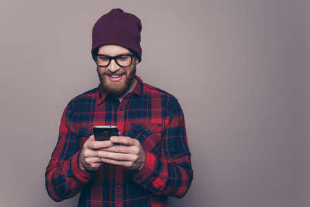Cheerful bearded smiling man in hat and glasses typing smsの写真素材