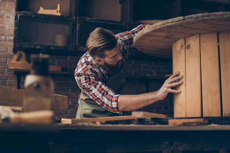 handsome joiner check wood.  Stylish young entrepreneur with beautyful hairstyle and saved glasses work at his workstation. he love his job and workplaceの写真素材