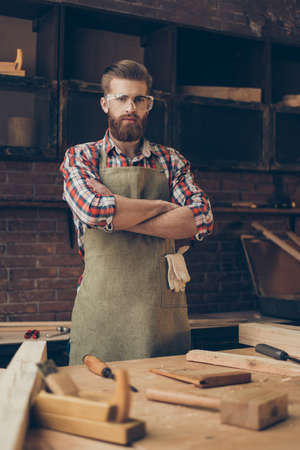young handsome  bearded craftsman with glasses and hairstyle crossed hands proud his job in workplace. He is successful entrepreneurの写真素材