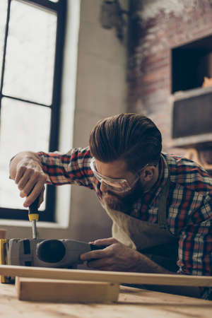 Closeup side view photo of handsome  worker repair instrument. Stylish young entrepreneur with brutal hairstyle and saved glasses work at his workplace. He love his jobの写真素材