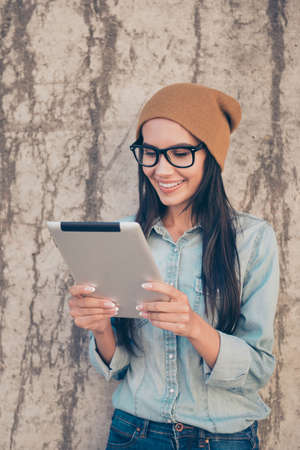 Pretty woman in hat and glasses using digital tablet to read newsの写真素材