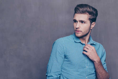 Thoughtful stylish man standing in front of gray background and touching his collarの写真素材