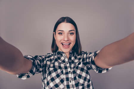 Young pretty happy woman in checkered shirt taking a selfie and looking at cameraの写真素材
