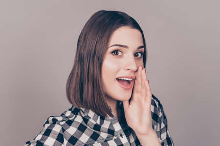 Young woman in checkered shirt holding hand near mouth and telling a secretの写真素材