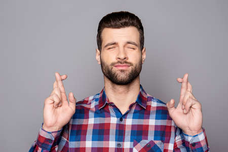 A portrair of a young man with crossed fingers and closed eyes praying for risky business