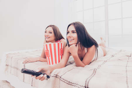Pretty girlfriends lying on bed with popcorn and watching interesting filmの写真素材
