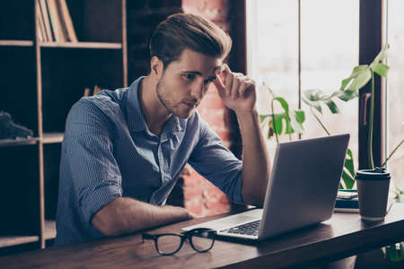 Young manager in checkered shirt reading information on the Internet on his computerの写真素材