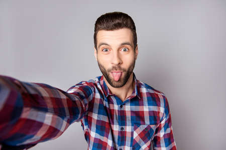 Playful stylish man isolated on gray background showing tongue and taking a selfieの写真素材
