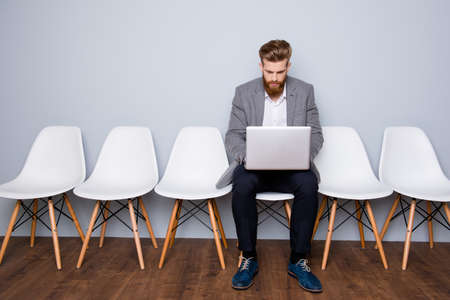 Portrait of young successful businessman sitting on a chair and working with laptopの写真素材