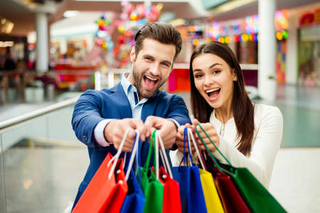 It's shopping and fun  time. Portrait of cheerful  successful happy young lovely couple holding  colored shopping bags and laughing in mall. Concept of consumerism, sale, rich life and people relationship.の写真素材