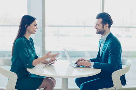 Smiling businessman and his young secretary discussing new project while sitting in airport and...