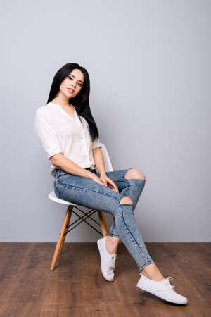 Young attractive calm woman posing on chair against gray backgroundの写真素材