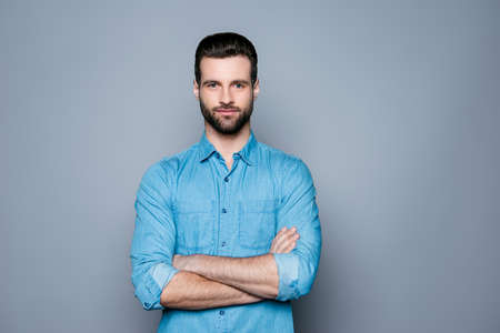 A portrait of young handsome smiling man in jeans shirt standing with crossed handsの写真素材