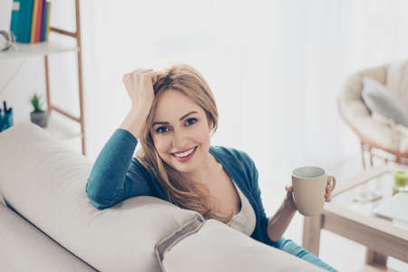 Young pretty cute woman enjoying coffee in the morning sitting on the sofaの写真素材
