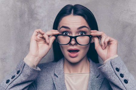 Portrait of smart young surprised and shocked businesswoman holding glasses and open mouth