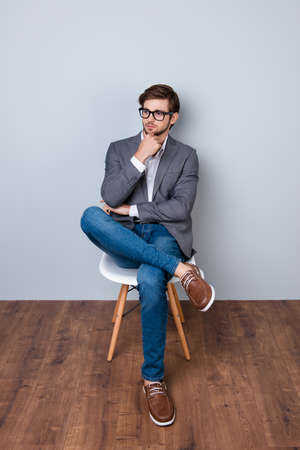 Confident cute smart business man with spectacles in formal wear sitting on the chair