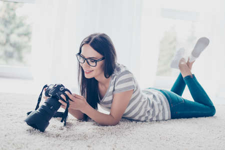 Young brunette pretty brunette photographer in spectacles checking photos on a camera while lying on the floor  at homeの写真素材