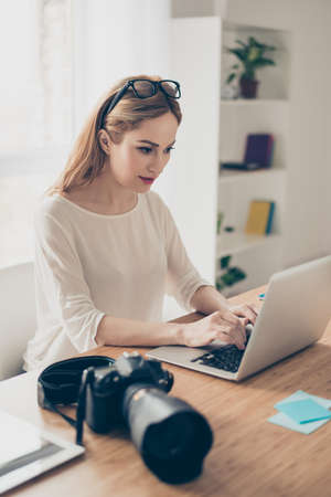 Young pretty cute  photographer working with laptop, download photo and retouch itの写真素材
