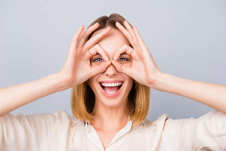 Happy laughing woman making binoculars using her hands against gray background