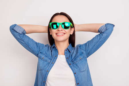 Portrait of happy young girl in bright sunglasses with hands behind the head on white backgroundの写真素材