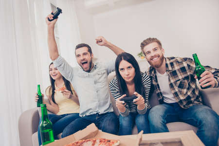 Young people having home party with video games, pizza and beer. They show different emotions because of who lost and who wonの写真素材