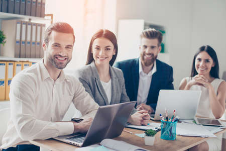 Close up of four successful young office workers looking straight and smiling, wearing smart formal...