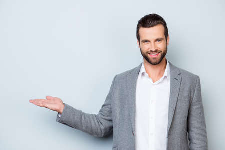 Handsome smiling young man in jacket showing on copyspace with his handの写真素材