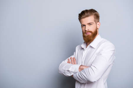 Half-profile portrait of serious confident bearded man keeping  crossed hands near copy space and looking at cameraの写真素材