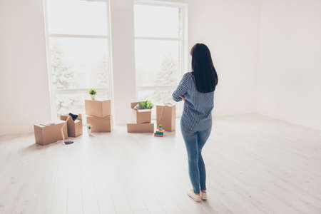 Dream come true! A start of new life! Brunette woman moved in to new light modern apartment and looking at boxes with her belongings, planning how she will organize the space hereの写真素材