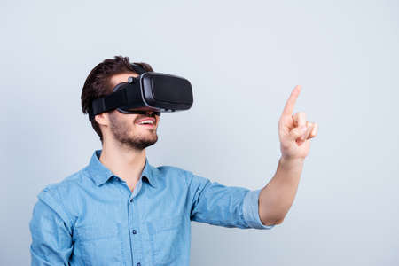 Happy young man is using vh headset glasses of virtual reality, pointing on sopmething with finger