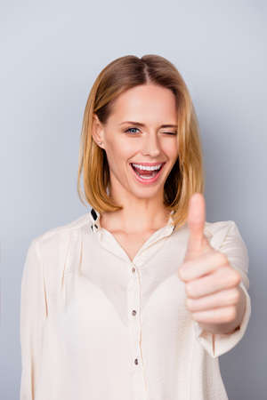 Attractive smiling woman in shirt giving a wink and showing thumb up on gray backgroundの写真素材