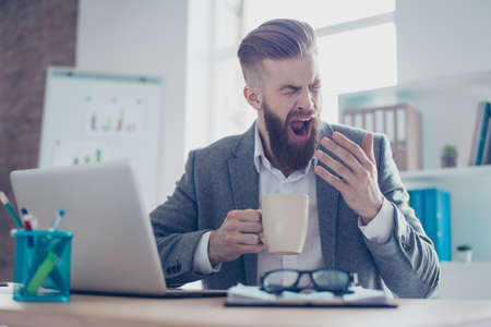 Portrait of a sleepy tired businessman snoozing and having a coffee at the work placeの写真素材