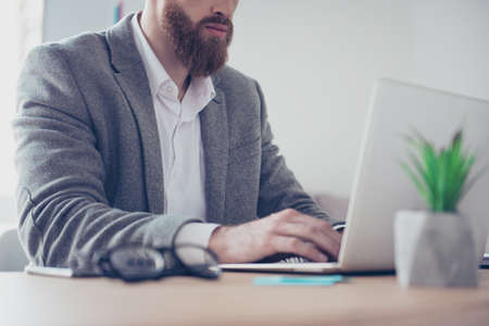 Close up cropped portrait of bearded businessman in suit typing on his laptop at the officeの写真素材