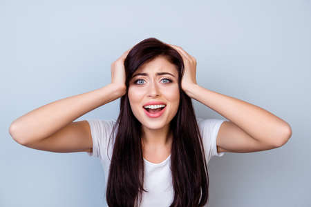 Close up portrait of young shocked woman  touching her head with hands against gray backgroundの写真素材