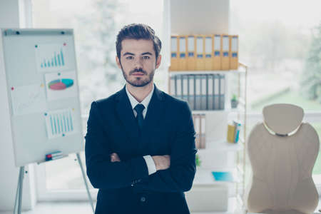 Concept of successful young confident businessman. Concentrated man with crossed arms standing in...