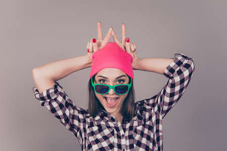 Portrait of young laughing woman in pink hat, sunglasses having fun and making v-sign over her headの写真素材