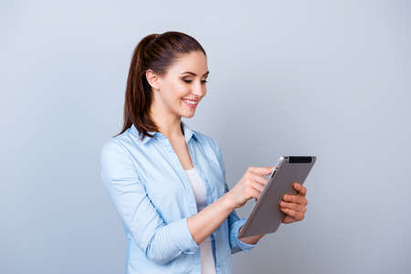 Nice-looking smiling woman in blue shirt chatting with her friends using digital tablet against gray...