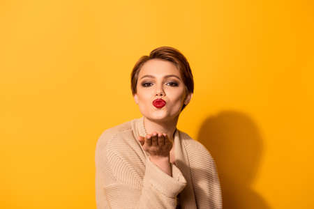 i send a for you cute young girl with nice make up wearing beige cardigan is standing on the bright yellow background and sends aの写真素材