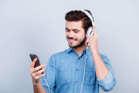 Excited young handsome man is listening to music on his pda with big white earphones, he looks at the screen of the phoneの写真素材