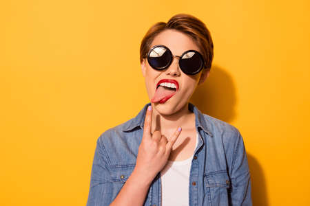 rock n roll portrait of a playful young stylish girl with tongue out. she is in a jeans shirt and...