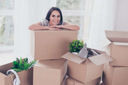 close up portrait of nice smiling brunette girl which put her hands and head on the box with her stuff, she is moving to new apartment. excited and can`t waitの写真素材