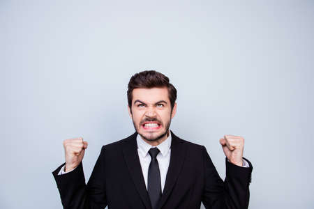 Young very angry man in black suit showing fists and looking up on copyspace over his head in rageの写真素材