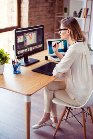 Vertical photo of attractive young photographer working with computer at the table and retouching with computerの写真素材