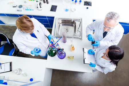 Top view of team work of three scientists, making tests with chemicals in flasks, making notes, all...