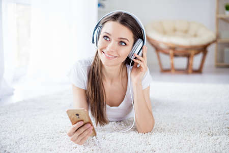 Cute dreaming young girl listening to music in headphones lying on the floor. She turned on her favorite playlistの写真素材